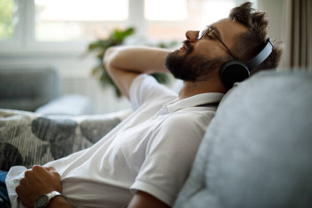 Young Smiling Man With Bluetooth Headphones Relaxing On Sofa