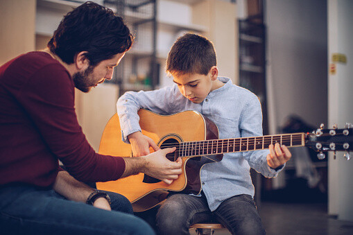 Two People, Man Guitar Teacher Working With Little Boy On Guitar Lessons.