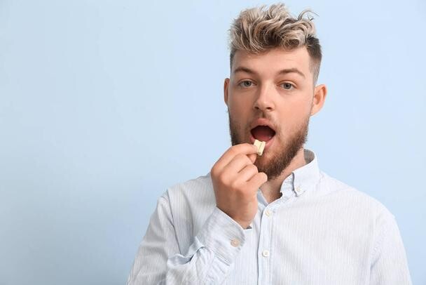 Young Man With Chewing Gum On Color Background